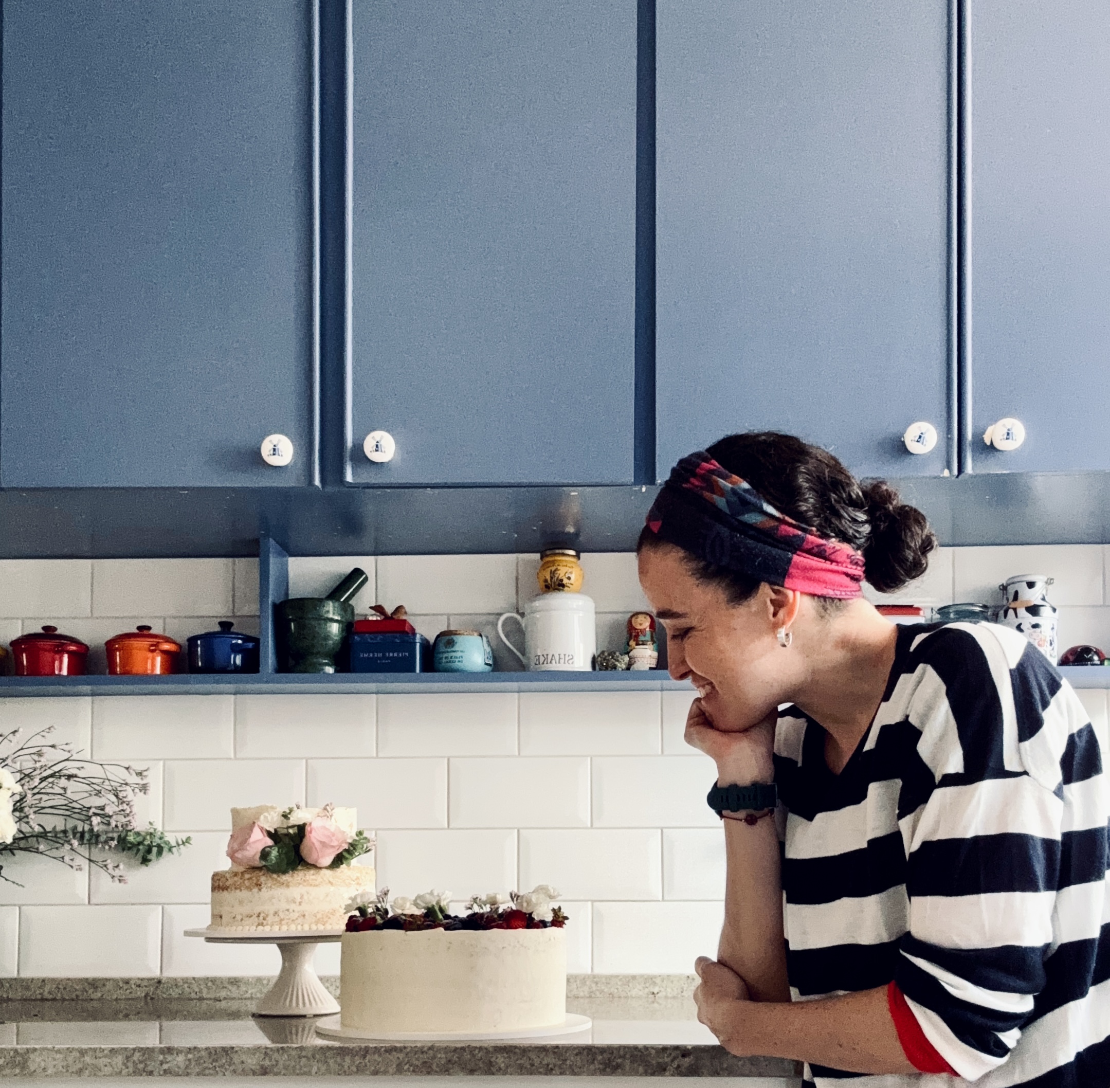 Ana observando bolos em uma cozinha com armário azul